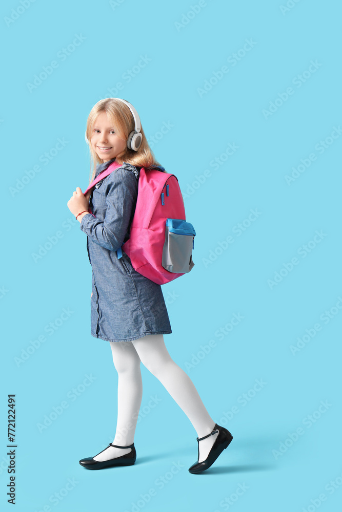 Cute schoolgirl with headphones and backpack on blue background