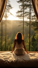 Poster - A woman is sitting on a bed in front of a window with trees outside