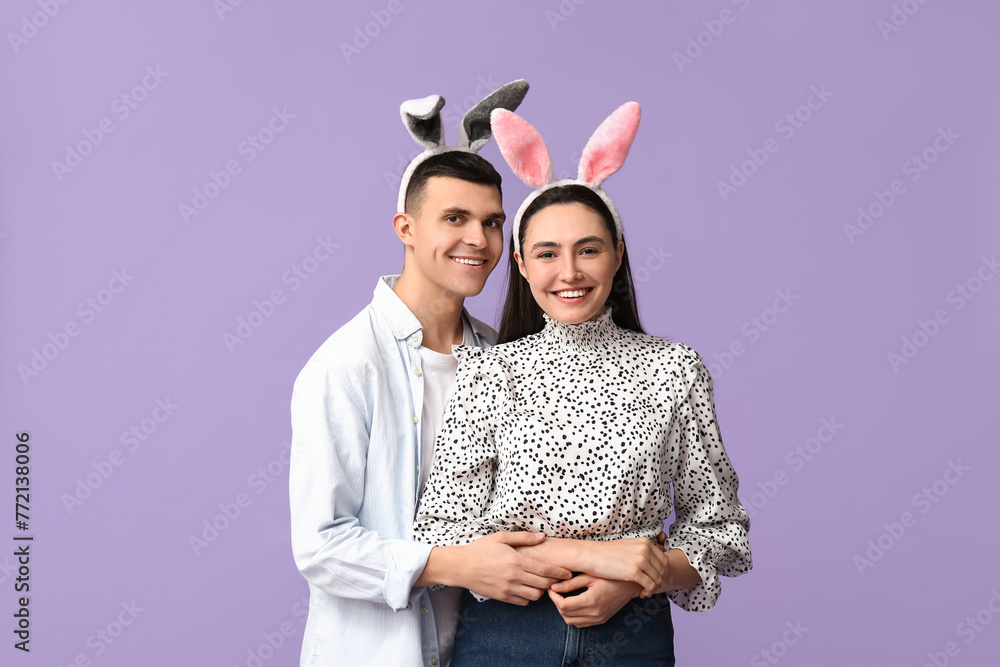 Happy young couple with Easter bunny ears on lilac background