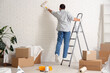 © Pixel-Shot - Handsome young man with paint roller painting wall during repair in new house