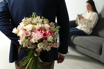 Canvas Print - Man hiding bouquet of flowers for his beloved woman indoors, closeup