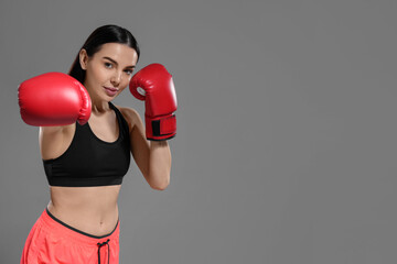 Canvas Print - Beautiful woman in boxing gloves training on grey background. Space for text