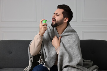 Canvas Print - Young man using throat spray at home