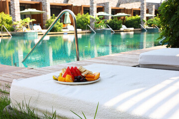 Wall Mural - Plate with fresh fruits on sun lounger near outdoor swimming pool. Luxury resort