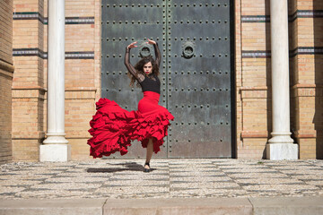 Wall Mural - Young, beautiful, brunette woman in black shirt and red skirt, dancing flamenco in front of an old, black metal door. Flamenco concept, dance, art, typical Spanish.