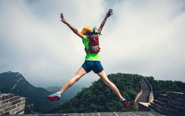 Wall Mural - Successful woman hiker jumping on great wall