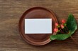 Mockup of a brown ceramic plate with a blank white card on a dark old wooden table with a branch of decorative berries close-up.