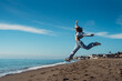 © sutulastock - A tanned young woman jumps in a blue suit, a brunette in a tracksuit, an active girl jumps cheerfully on the sea coast. Athletic girl in a tracksuit jumping on the sand