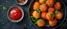 A Black Plate Topped With Deep Fried Potato Balls Filled With Melted Mozzarella Cheese, Alongside A Bowl Of Ketchup.