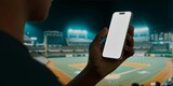 Fototapeta Sawanna - A hand holds a smartphone with a blank screen at a baseball stadium