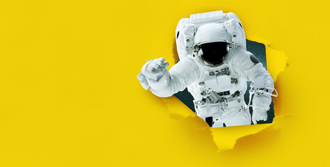 Wall Mural - space man astronaut tears paper from hole, concept. yellow banner for design and text. creative idea