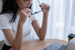 © Wasana - Asian woman wearing glasses works seriously on laptop in bright room.
