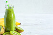 Kiwi and banana green smoothie in a glass bottle with fresh fruits on white wooden background with copy space. Healthy summer diet drink