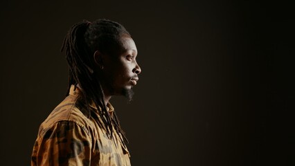Wall Mural - Smiling person posing in studio with black background, feeling confident wearing dreads and camo clothing. Cool guy with trendy hair acting stylish on camera, attractive man. Handheld shot.