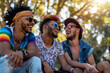 Group of LGBT friends at the park, three interracial friends laughing in their free time under a tree during gay pride