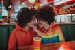 Gay couple eating fast food, two lesbian women in a date in a bar with clothes of LGBT colours during pride