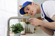 Smiling plumber repairing faucet with spanner in kitchen