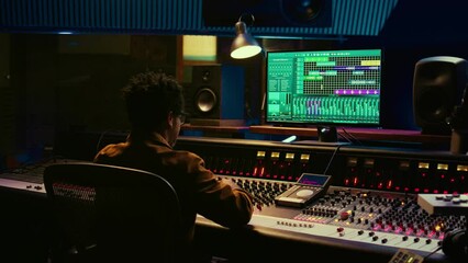 Fototapete - Audio expert counts down for artist singing in vocal booth, recording tracks to edit them after in post production. Producer operates mixing console and buttons or sliders, control room. Camera B.