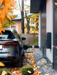 © Olga - Electric vehicle EV car is being charged from a wallbox on a contemporary modern building house. Concept home charging for electric vehicles