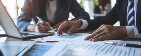 Close-up view of business professionals' hands working with financial reports and a laptop on a desk in a corporate setting.