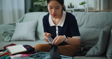 Fototapeta Mapy - Front view of Asian teenager woman sitting on sofa packing travel luggage with personal items for traveling trip, Preparation travel suitcase at home.