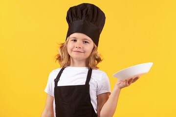 Wall Mural - Cute kid boy cook with cooking plate. Child chef cook, studio portrait. Kids cooking. Teen boy with apron and chef hat.