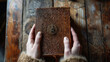 A pair of hands holding a locked leather journal its pages filled with cryptic symbols and clues to an unsolved mystery. . .