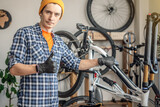 Fototapeta  - A male bicycle mechanic in the workshop disassembles a mountain bike and repairs it. Maintenance concept, preparation for the new season