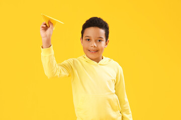 Wall Mural - Little African-American boy with paper plane on yellow background. Children's Day celebration