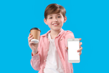 Canvas Print - Little boy with cup of cocoa and mobile phone on blue background. Children's Day celebration