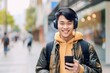 Asian man is listening to music on smartphone with headphones outdoors