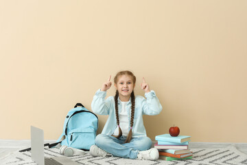 Wall Mural - Little girl with books, apple and backpack pointing at something near beige wall. Children's Day celebration