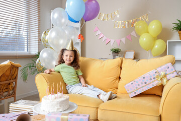 Poster - Cute little girl sitting on sofa in party hat with balloons, cake and decorations for birthday at home