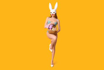 Wall Mural - Sexy young woman in bunny mask with basket for Easter on yellow background