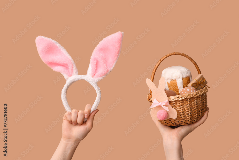 Female hands holding basket with Easter cake and bunny ears on beige background
