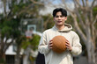 © Prathankarnpap - Handsome man holding ball with both hands and smiling at camera, standing on the playground