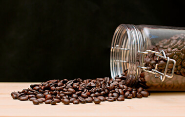 Raw coffee beans in a glass bottle spill out onto a wooden table in the corner, side view. coffee lover portrait