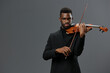 Elegant African American man playing violin in black suit on gray background for musical performance concept
