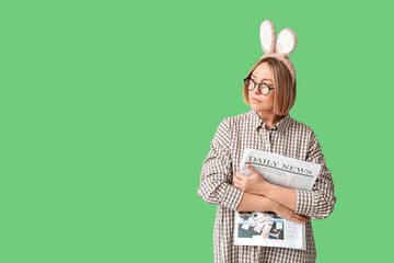 Wall Mural - Adult female manager in bunny ears with newspaper on green background. Easter celebration