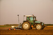 Green tractor seeding soil with planter in agricultural field during golden hour