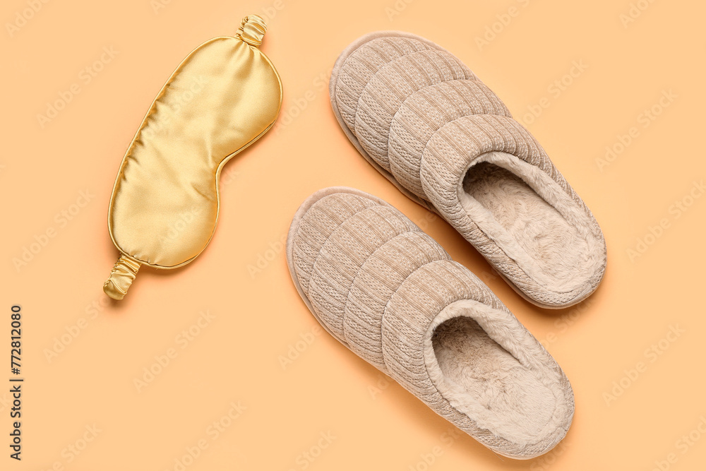 Pair of beige soft slippers and sleep mask on beige background. Top view