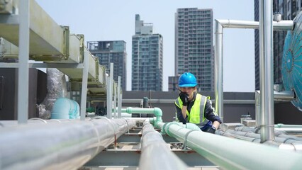 Wall Mural - Asian woman engineer in safety uniform working and speaking on two way radios at outdoor construction site rooftop. Industrial technician worker maintenance checking building exterior plumbing systems