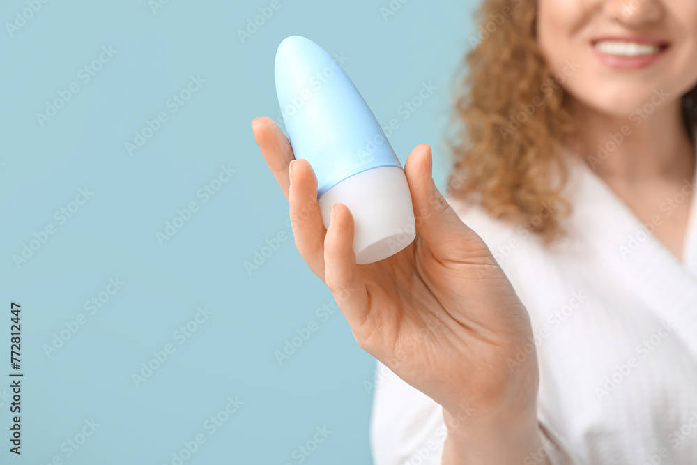 Young woman with deodorant on blue background, closeup