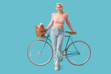Fototapeta Panele - Beautiful young woman with bicycle and bouquet of flowers on blue background