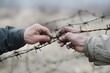 closeup of two hands pulling apart a barbed wire gap