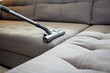 individual vacuuming a modern couch with upholstery nozzle