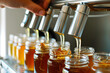 person filling small jars with honey using a stainless steel tap