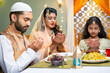Indian Muslim family with kid praying at ramadan iftar dinner before eating at home - concept of traditional festival culture, rmzan kareem and family bonding