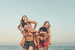 Two couples share laughter with piggyback rides on the beach, embodying the spirit of a carefree and joyful vacation by the sea - beach joy - copy space in the sky