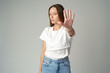 © fotofabrika - Portrait of a young woman standing with outstretched hand showing stop gesture on gray background